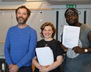 Three performers pose for the camera holding show scripts